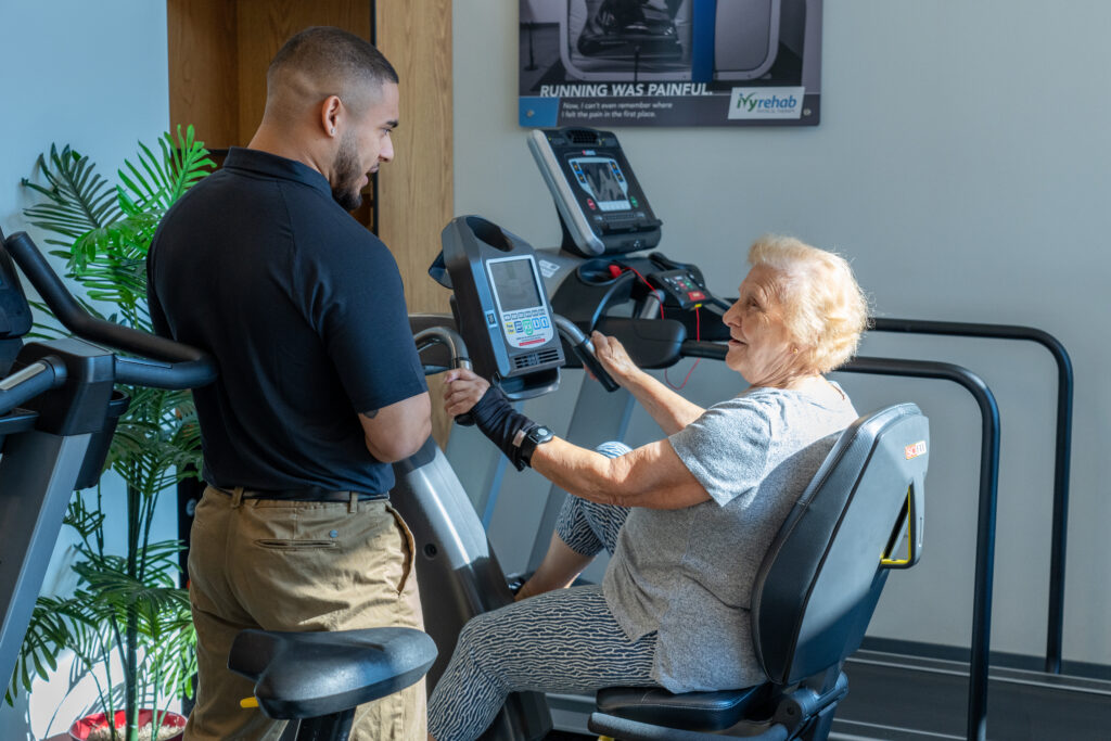 Physical therapist assisting an older adult with exercise equipment during a therapy session