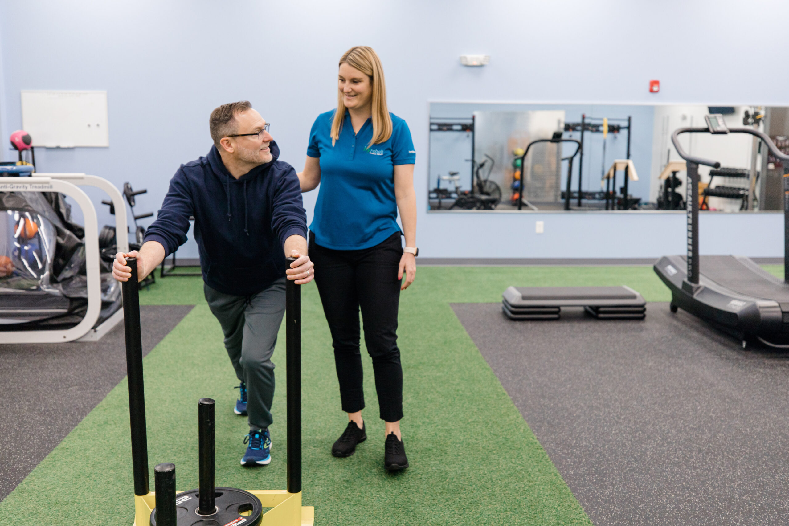 Clinician supervising an employee pushing a weighted sled during an early intervention conditioning exercise