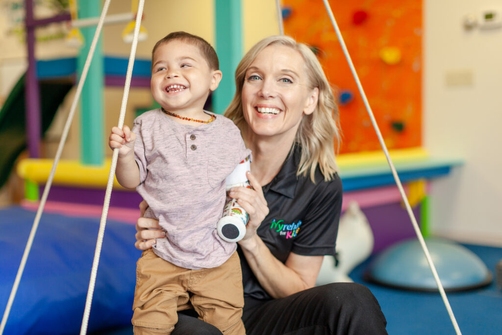 Pediatric therapist holding a young boy on a suspended swing in a therapy gym