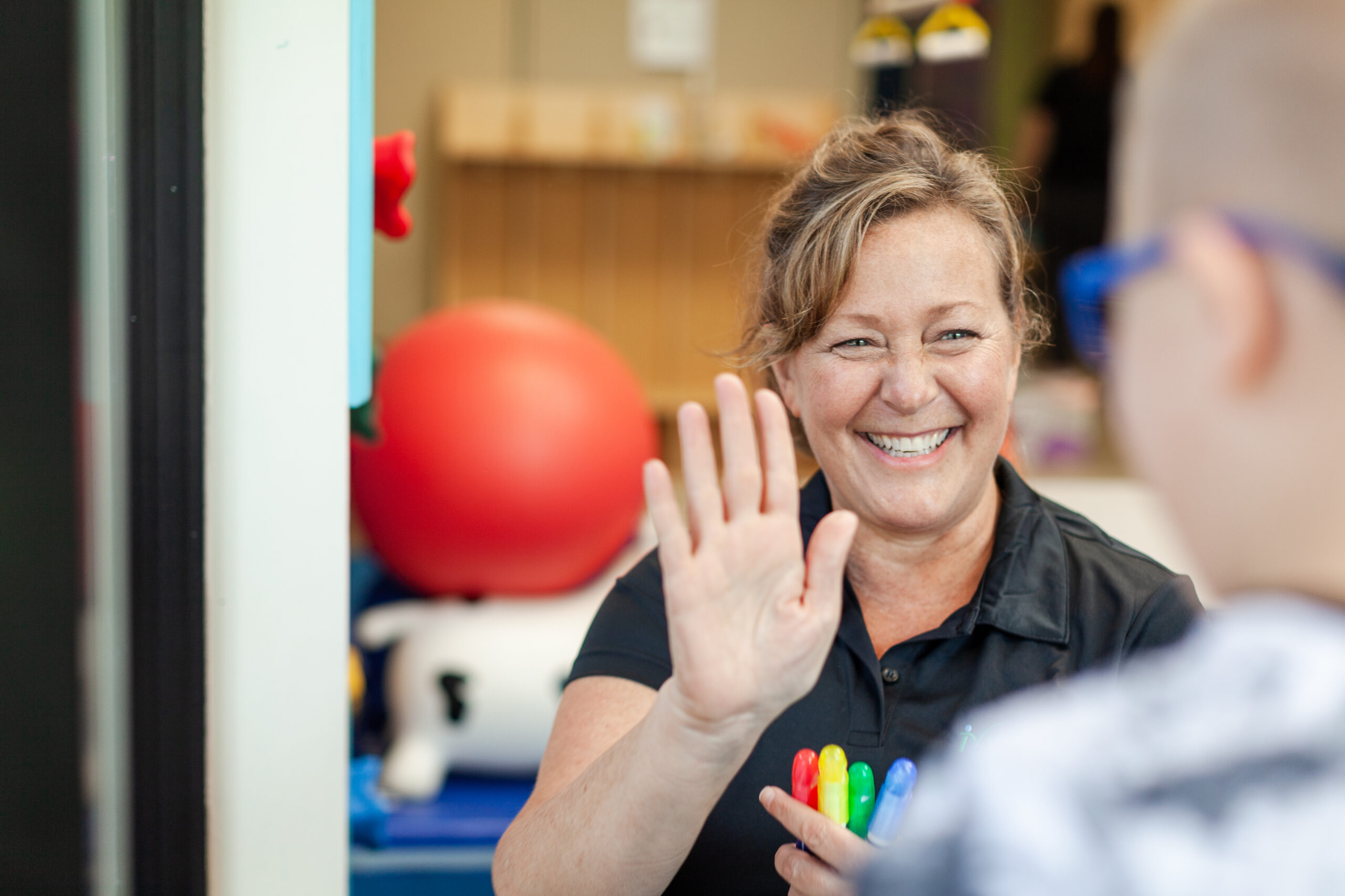 Physical therapist smiling and waving to a patient during a therapy session