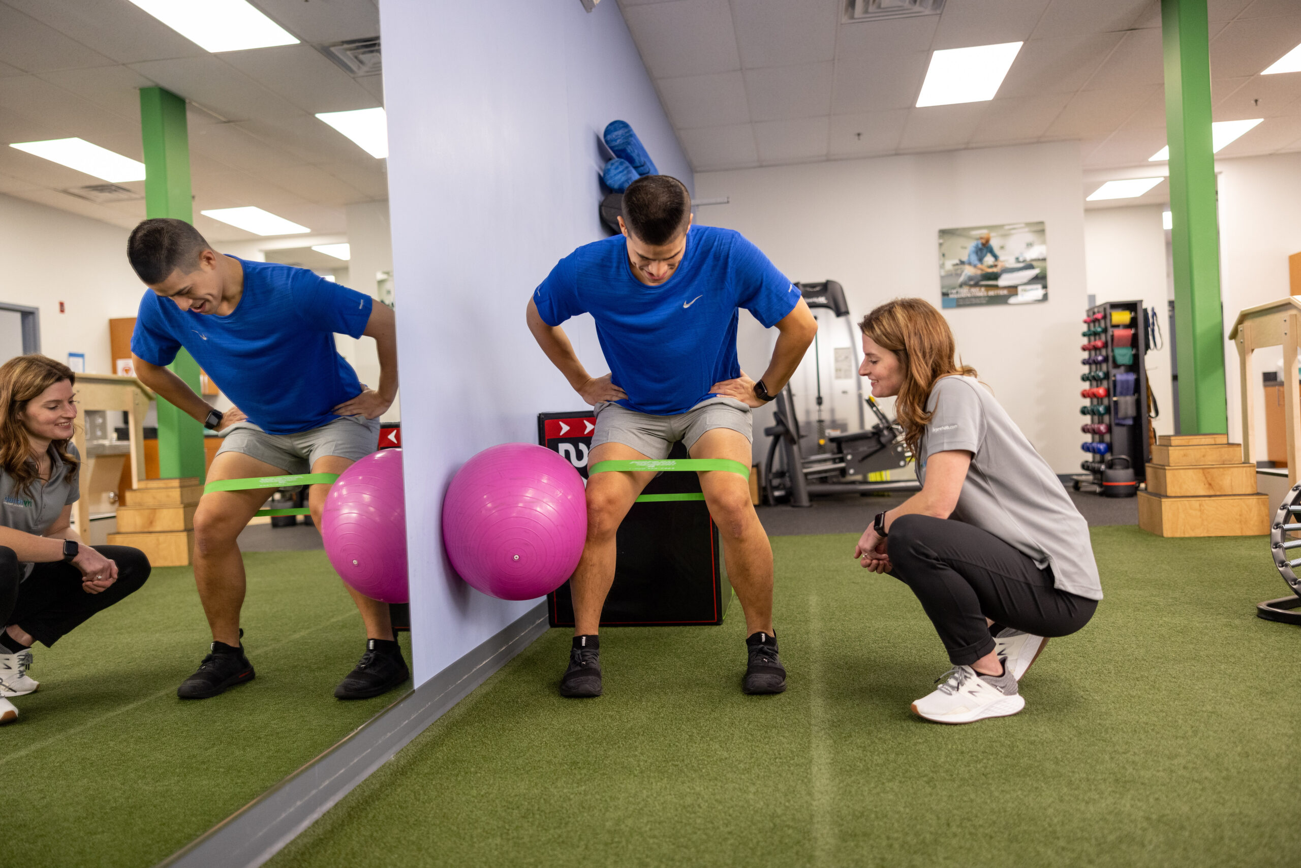 Therapist coaching two patients through a resistance band exercise with stability balls in a clinic gym