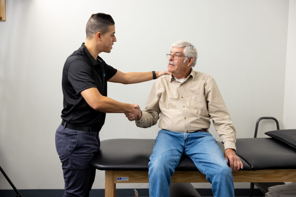 Physical therapist shaking hands with a patient who is sitting on a bench