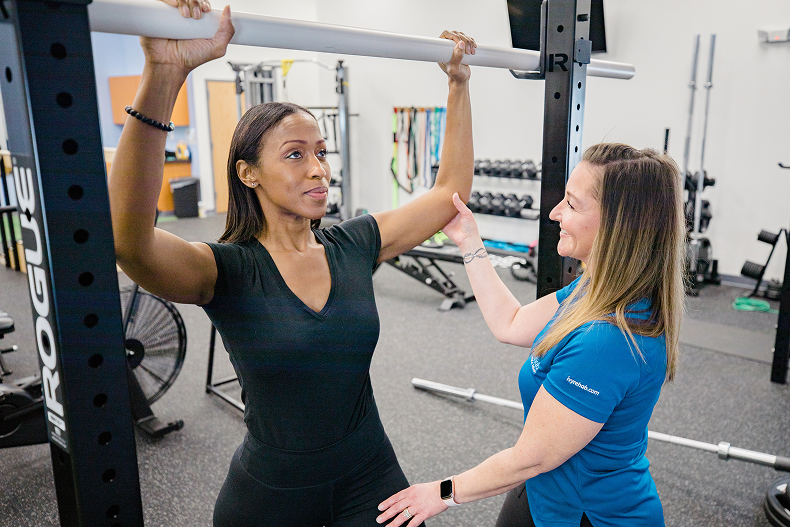 Physical therapist helping a patient with an overhead arm exercise using a squat rack bar