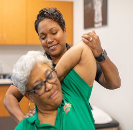 Therapist assisting a patient with a shoulder and neck stretch in the clinic