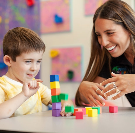 Pediatric therapist helping a young boy build motor skills with colorful blocks during a therapy session